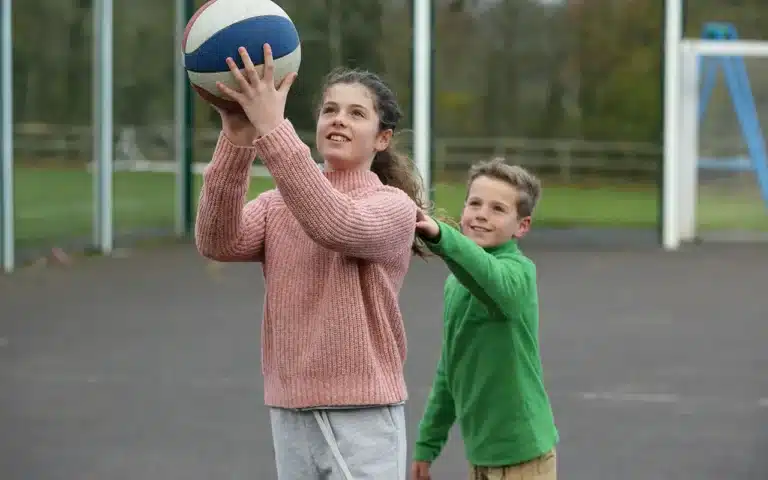 Fille et garçon jouant au basketball en extérieur, moment de sport et d’amusement.