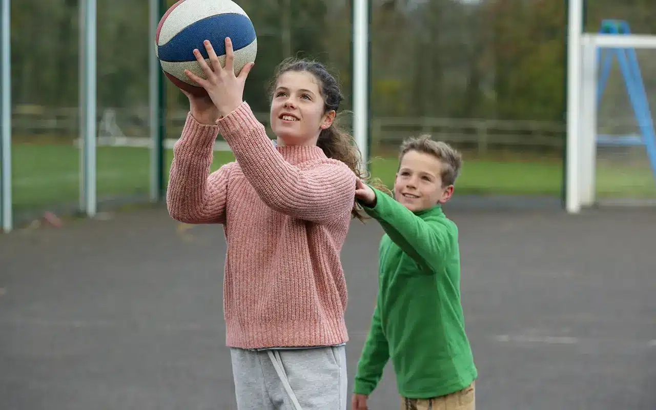 Fille et garçon jouant au basketball en extérieur, moment de sport et d’amusement.